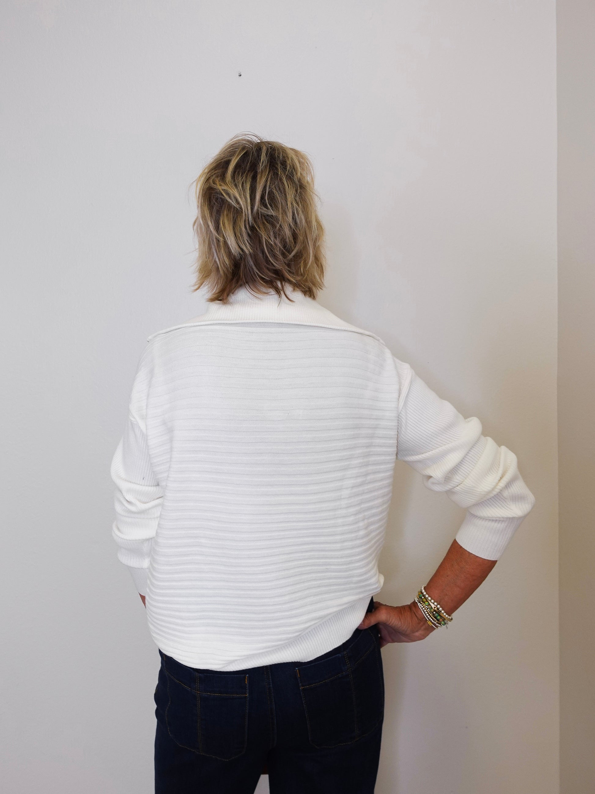 Person wearing a white ribbed sweater against a plain background
