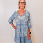 Woman wearing a blue embroidered dress against a white wall