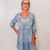 Woman wearing a blue embroidered dress against a white wall