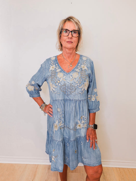 Woman wearing a blue embroidered dress against a white wall
