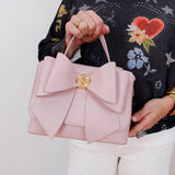 Person holding a pink handbag with a decorative bow, wearing a black sweater with floral patterns.