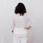 Person wearing a white textured sweater and pants against a plain white wall.