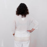 Person wearing a white textured sweater and pants against a plain white wall.