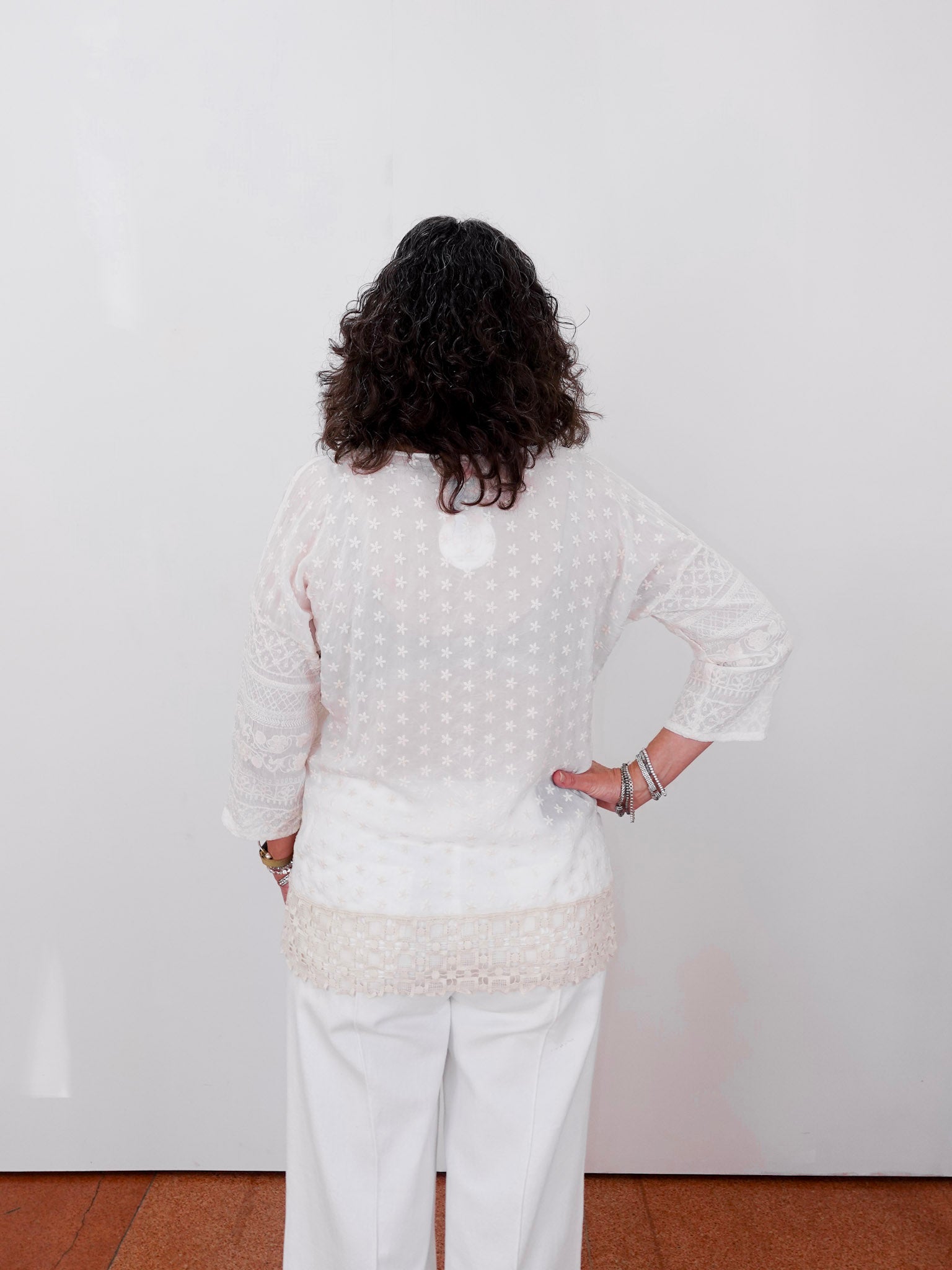 Person wearing a white textured sweater and pants against a plain white wall.